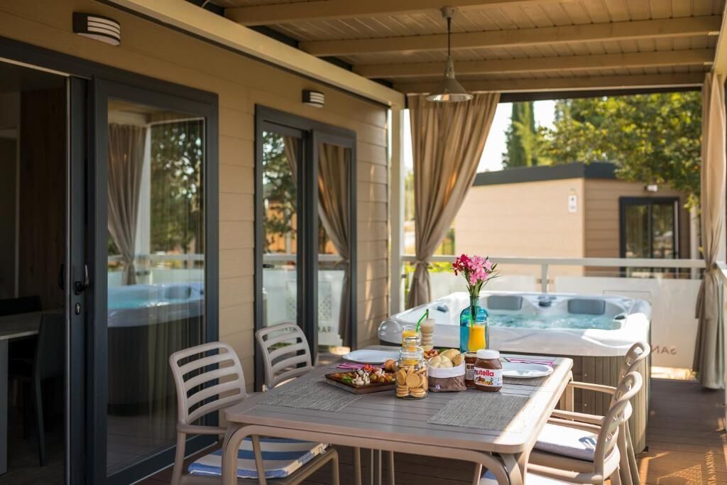 A covered outdoor dining area with a table set for breakfast, a hot tub, and a glass door leading to a pool.