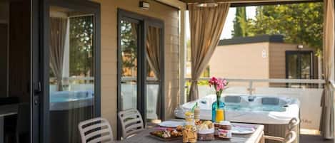 A covered outdoor dining area with a table set for breakfast, a hot tub, and a glass door leading to a pool.