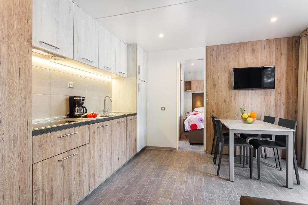 Een moderne keuken met houten kastjes, een koffieapparaat en een eethoek met een tafel en stoelen.