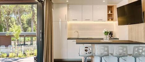 A modern kitchen with a large window, white cabinets, a black countertop, and three bar stools.