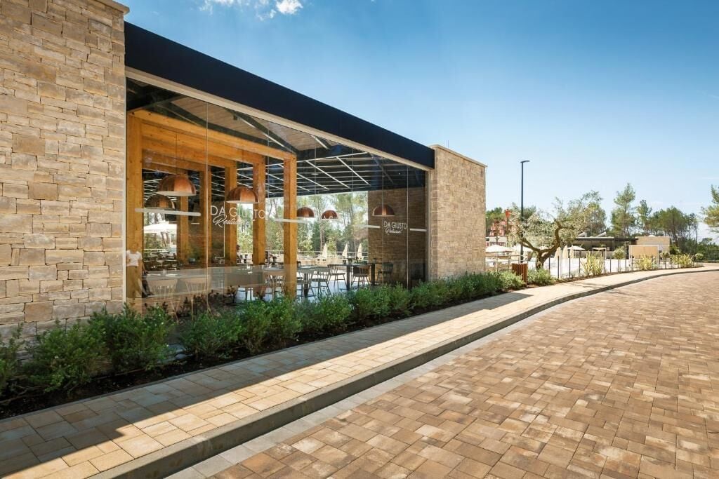 A modern building with a brick facade, large glass windows, and an outdoor seating area with tables and chairs.