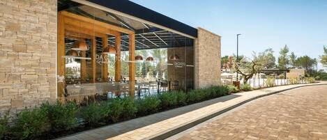 A modern building with a brick facade, large glass windows, and an outdoor seating area with tables and chairs.