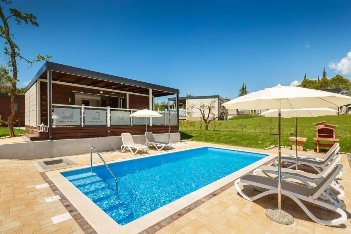 A modern pool area with a clear blue pool, lounge chairs, and umbrellas.
