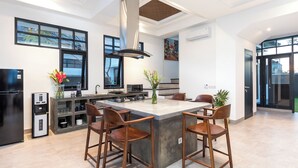 A modern kitchen with a central island, bar stools, a built-in oven, and a large window. - Villa Sakayana (Canggu)