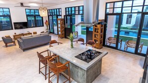 A modern kitchen with a central island, large windows, and a dining area with wooden chairs. - Villa Sakayana (Canggu)