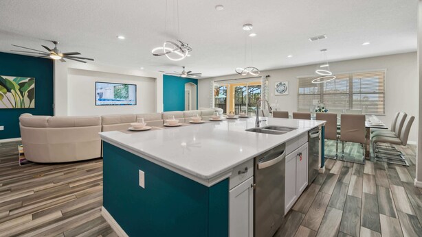 Una cocina moderna con una isla central, una zona de comedor con una mesa larga y una sala de estar con un sofá.