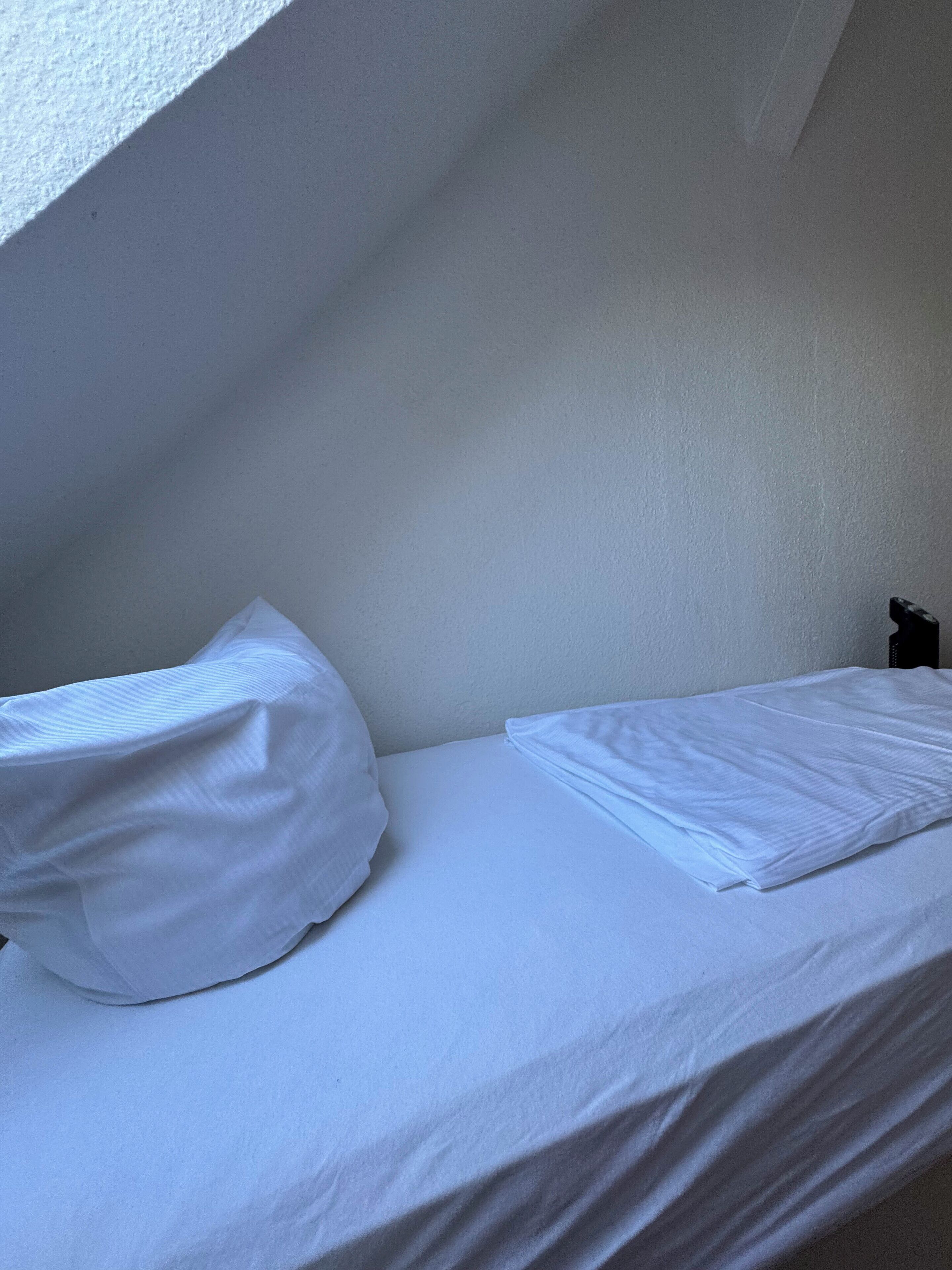 A small, single-bed room with white bedding and a sloped ceiling.