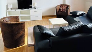 Ein modernes Wohnzimmer mit einem schwarzen Ledersofa, einem braunen Sessel, einem weißen Couchtisch und einem Flachbildfernseher auf einer weißen Kommode.