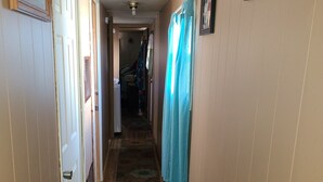 A narrow hallway with wooden floors, a patterned carpet, and a blue curtain.
