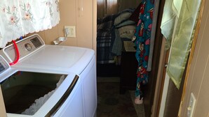 A compact laundry area with a washing machine, a small table with a phone, and a bed with a floral bedspread.