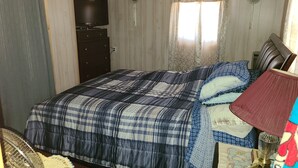 A bedroom with a bed, a dresser, a television, and a window with curtains.