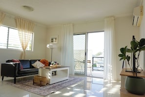 A modern living room with a black leather sofa, a white coffee table, and a large potted plant. - Located in the heart of Indooroopilly (Indooroopilly)