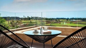 A balcony with a glass table and chairs, overlooking a golf course and distant buildings. - Villa Blanchette  (Marrakech)