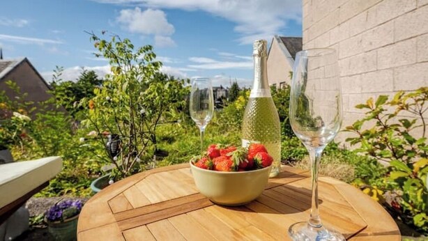 Ein runder Holztisch mit einer Schale Erdbeeren, einer Champagnerflasche und zwei Gläsern.