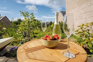 A round wooden table with a bowl of strawberries, a bottle of champagne, and two glasses. - Riverside Garden Apartment with lovely River Tay views and parking 

 (Perth)