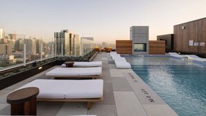 Área de piscina no terraço com espreguiçadeiras e vista para o horizonte da cidade.