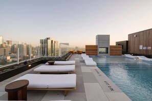 A rooftop pool area with lounge chairs and a view of the city skyline.