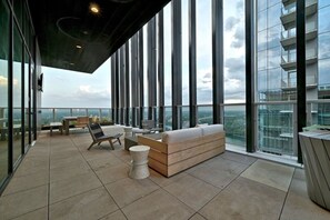A spacious balcony with a seating area, large windows, and a city view.