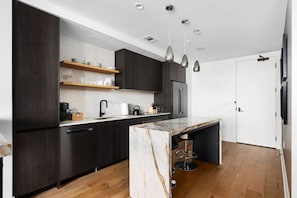 Cozinha moderna com armários escuros, bancada de mármore e iluminação pendente.