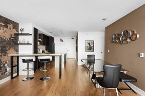 A modern kitchen with a bar area, a dining table with chairs, and a view of the cityscape through the window.