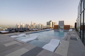 Piscina no terraço com espreguiçadeiras e vista para o horizonte da cidade.