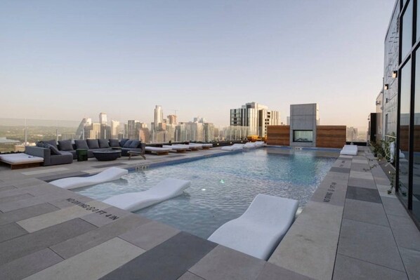 A rooftop pool with lounge chairs and a city skyline view.