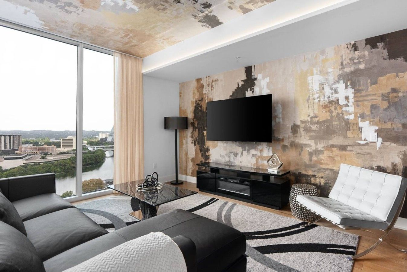 A modern living room with a large TV, a sofa, a coffee table, and a view of a cityscape through large windows.