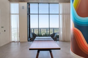 Amplo quarto com uma grande janela, uma mesa de conferência, duas cadeiras e uma escultura abstrata colorida.