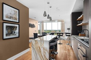 A modern kitchen with a marble island, bar stools, and a dining area with a view.