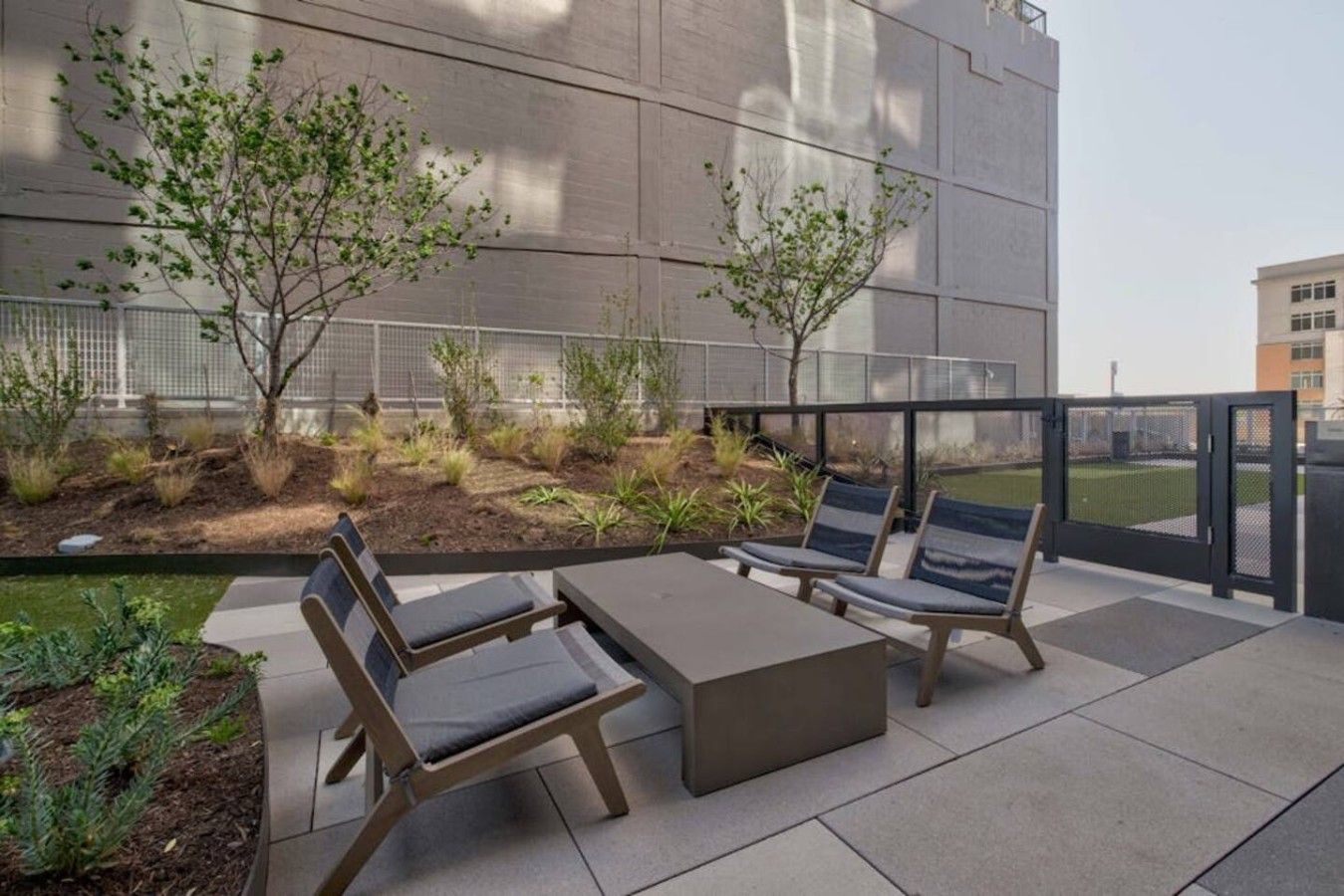 Un espace extérieur aménagé avec une table et des chaises, entouré d’un jardin où poussent différentes plantes et arbres.