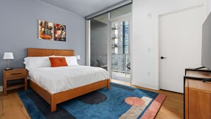 Quarto moderno com cama de madeira, tapete azul e porta de vidro que dá para uma varanda.