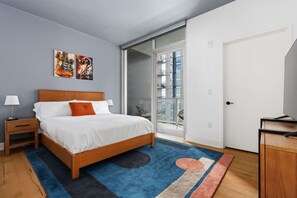 A modern bedroom with a wooden bed, a blue rug, and a glass door leading to a balcony.