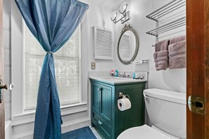 A bathroom with a toilet, a sink with toiletries, a mirror, and a towel rack.