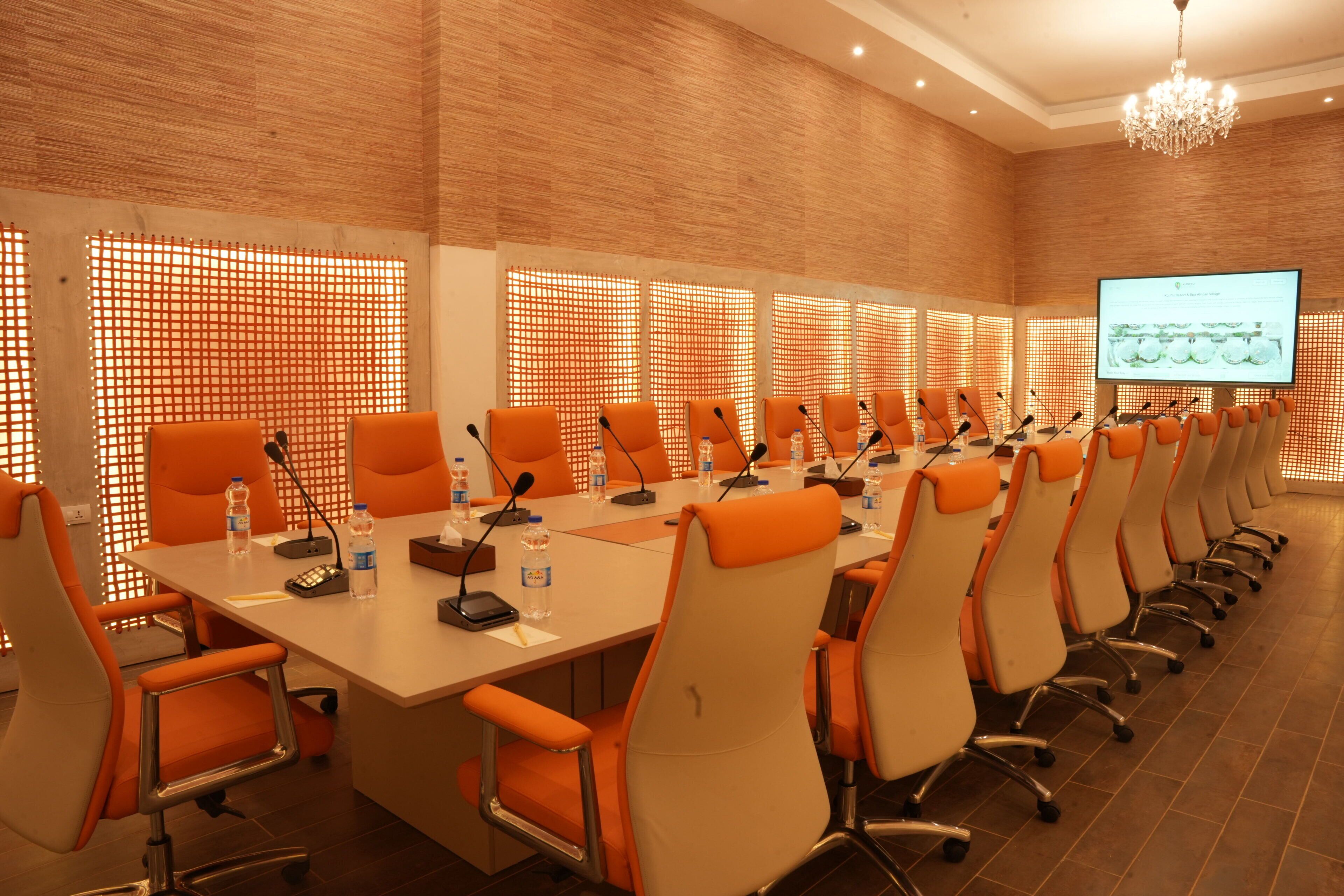 A conference room with a long table, multiple chairs, microphones, and a projector screen.