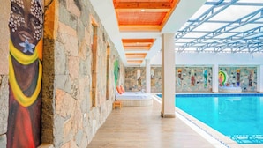 A swimming pool area with stone walls, a mural, and a ceiling with wooden beams.