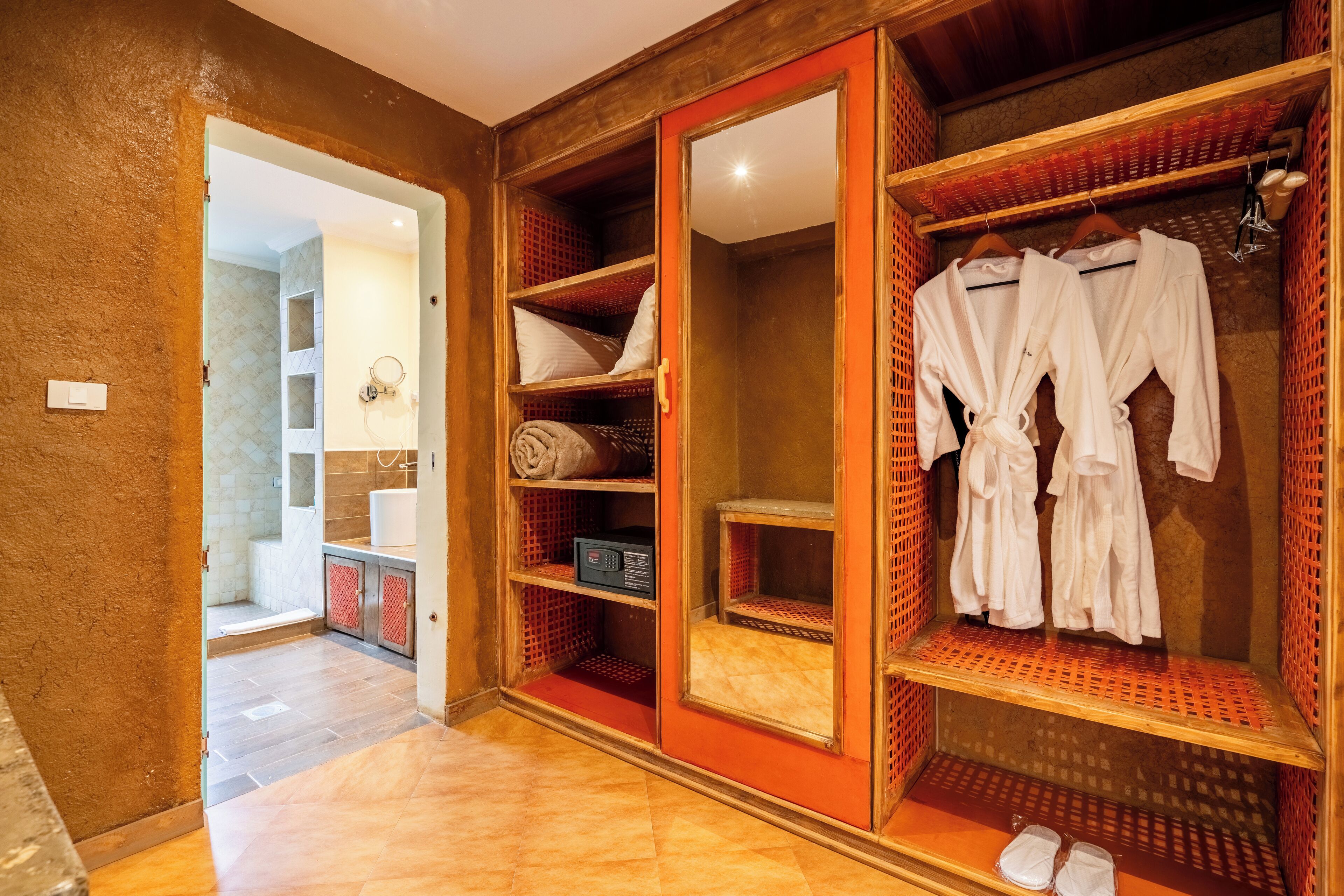 A hotel room with a wooden wardrobe, a mirror, and a shelf with towels and robes.
