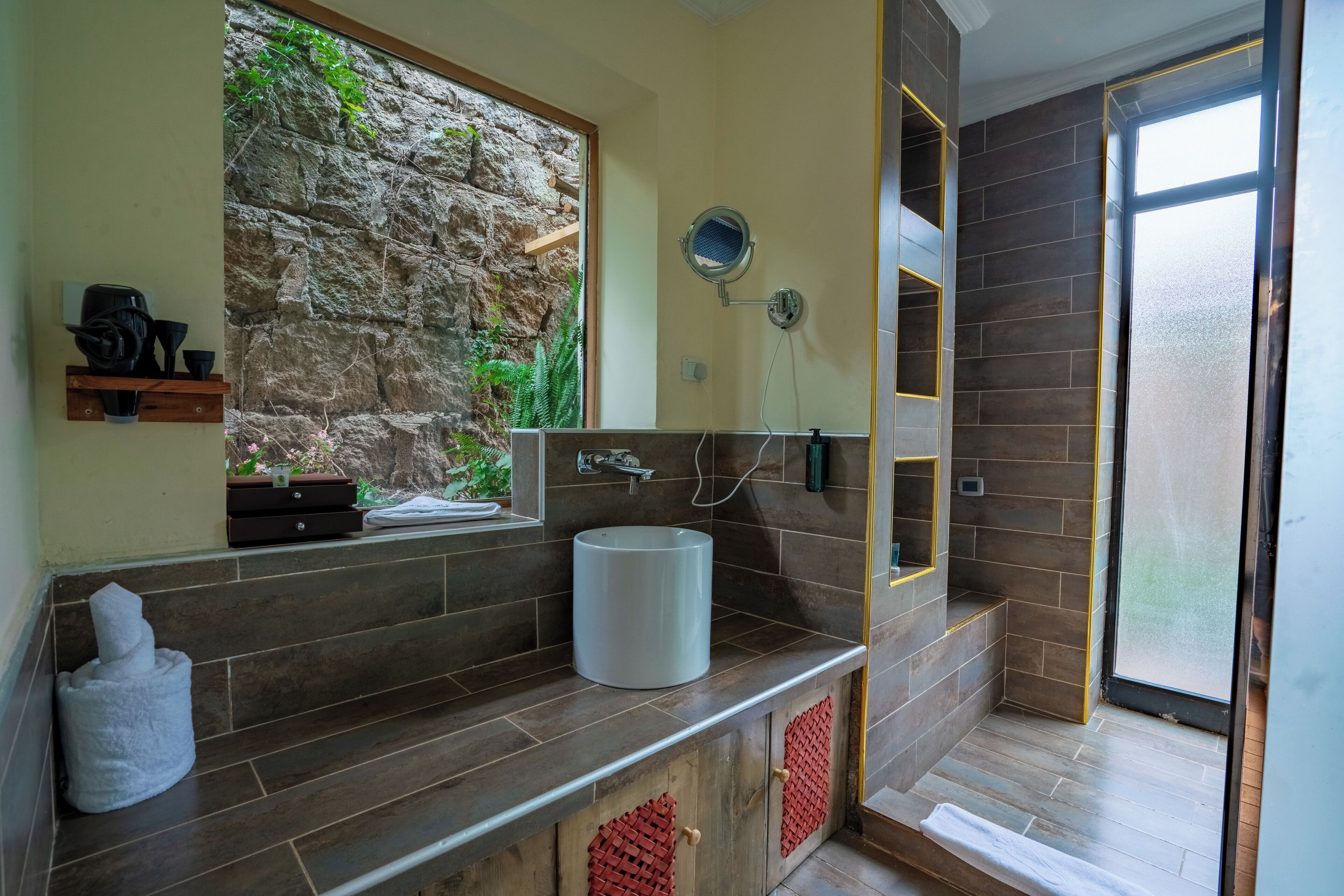 A bathroom with a stone wall, a sink, a mirror, and a shower area.