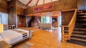 A spacious room with a large bed, a fireplace, a sofa, and a staircase.