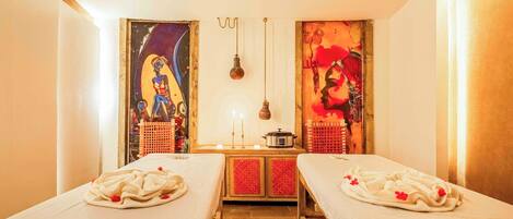 A room with two beds, a small table with candles, and artwork on the walls.
