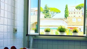 A kitchen with a window overlooking a building with potted plants and a tree. - Cozy house with balcony for couples 5 minutes from St. Peter's Basilica (Roma)