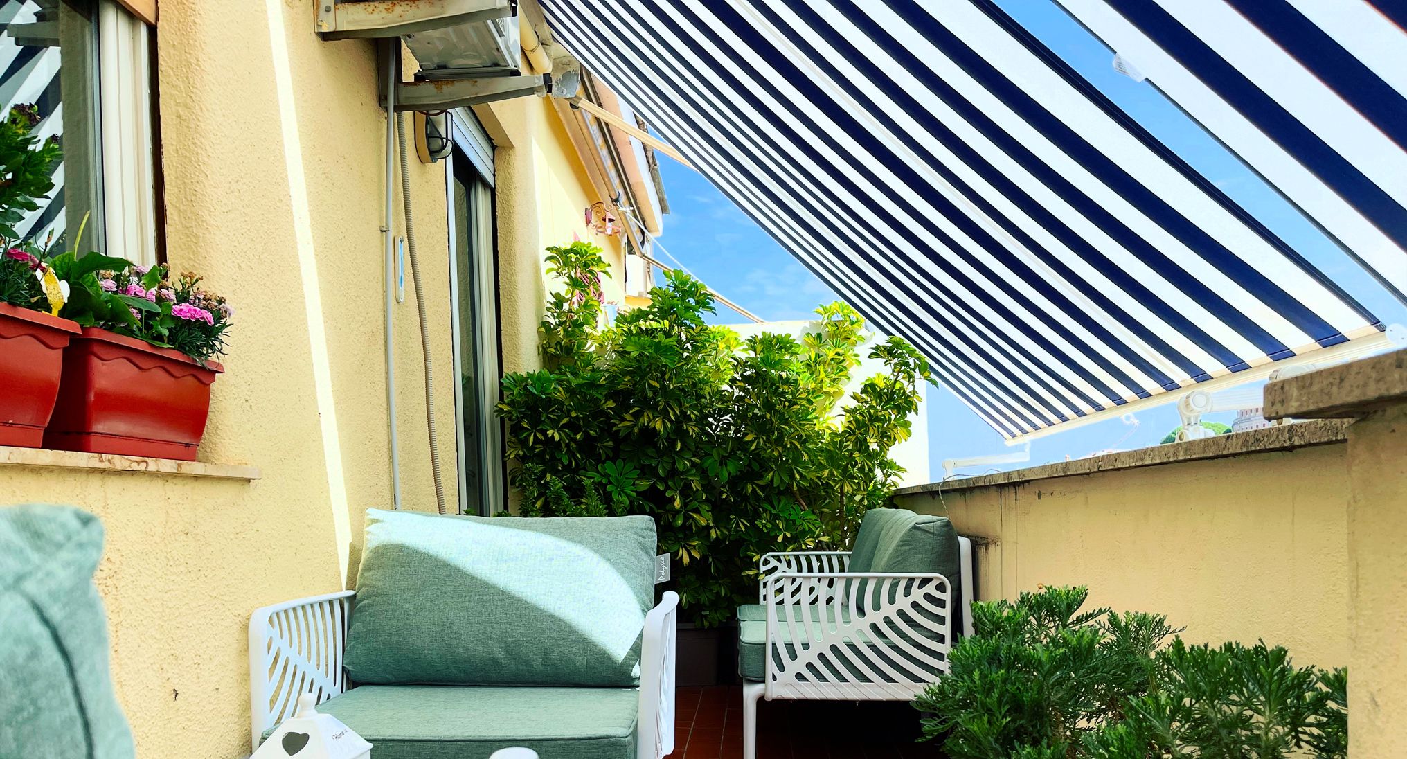 A patio with two white chairs, a small table, and a potted plant.