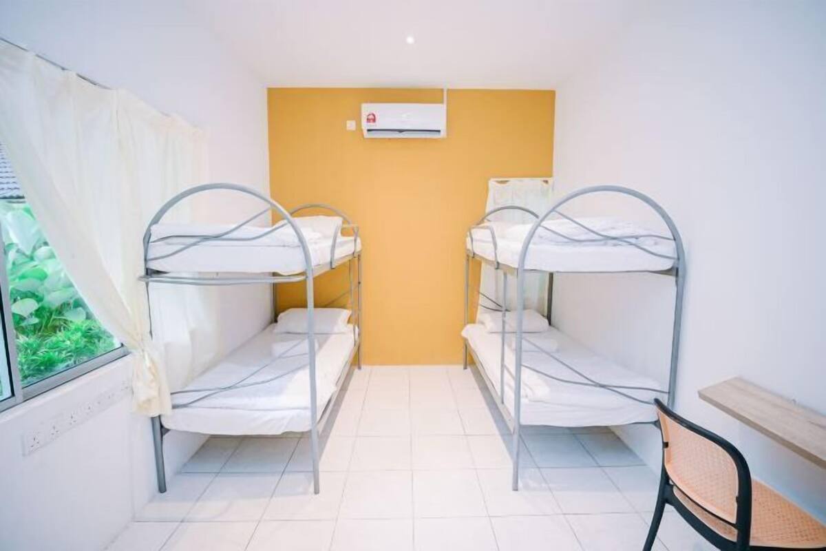 A dormitory room with bunk beds, a window with curtains, and an air conditioning unit on the wall.