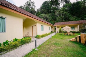 Una hilera de edificios de una sola planta con techo de tejas, un sendero pavimentado y un área ajardinada con plantas y mobiliario exterior.