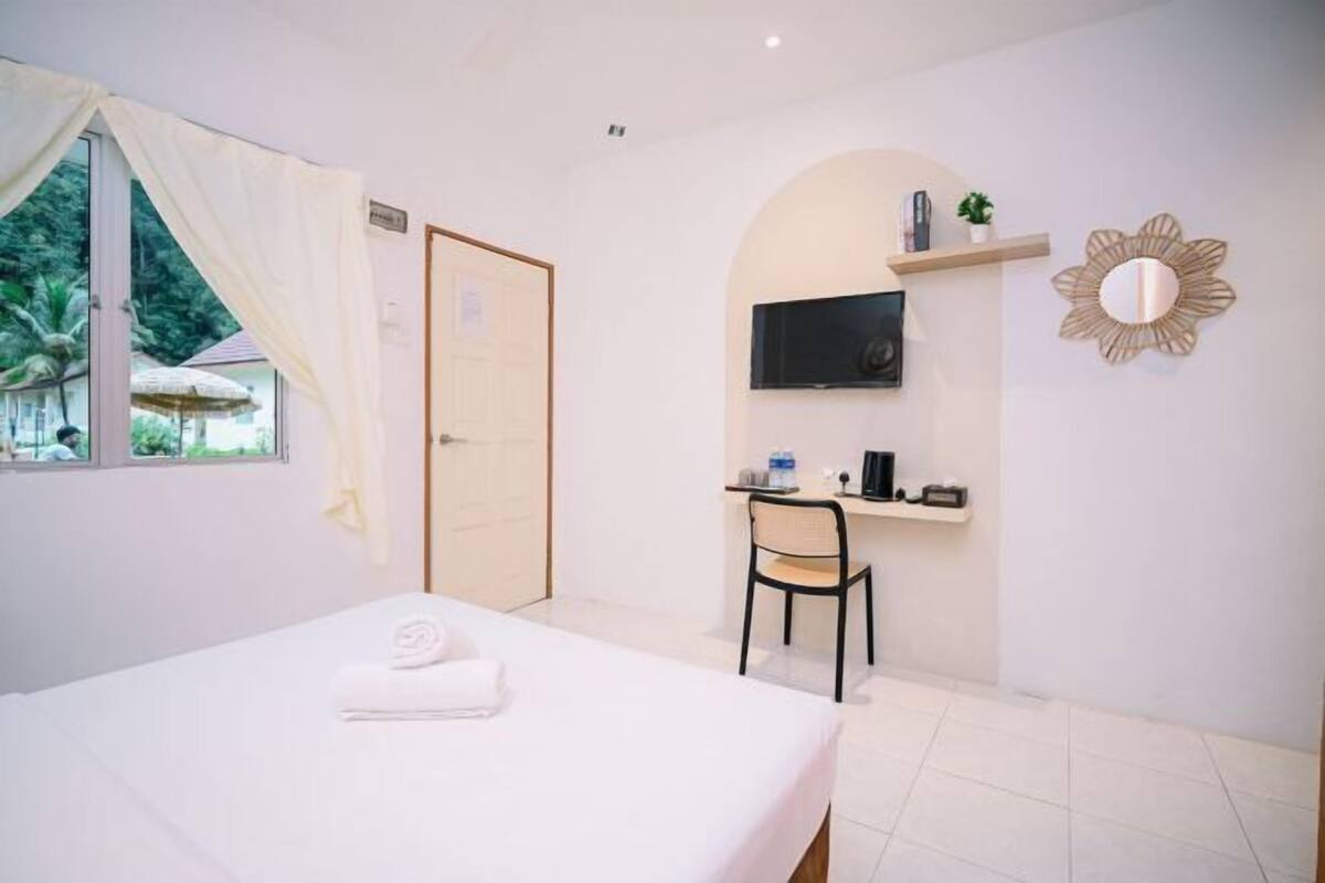 A hotel room with a bed, a desk, a chair, a TV, and a window with curtains.