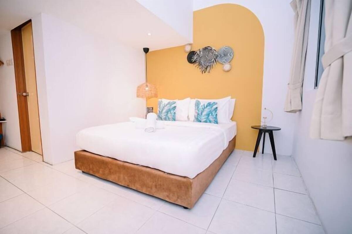 A modern bedroom with a bed, a small bedside table, a wall art piece, and a door.