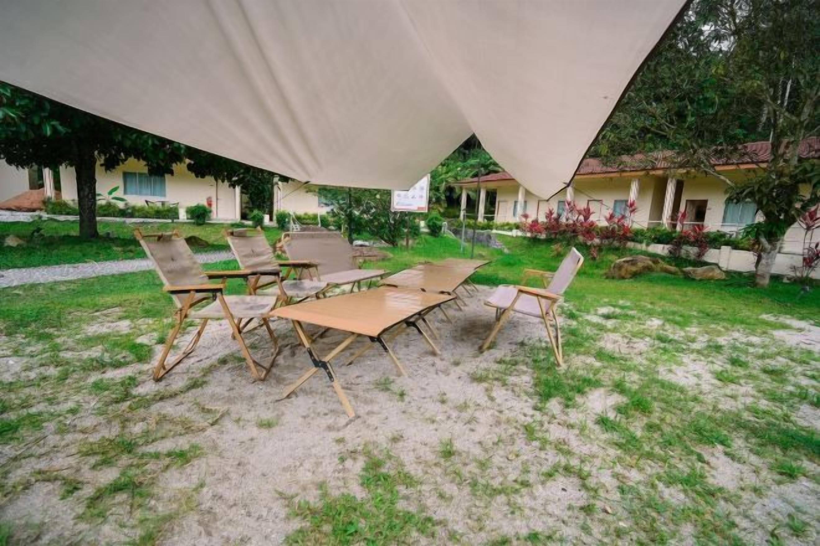 Un área de estar al aire libre con una mesa y sillas, una carpa sobre la cabeza y un jardín con césped y plantas.