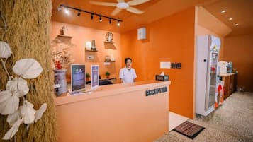 Un área de recepción con recepcionista, un mostrador, un ventilador de techo y un refrigerador.