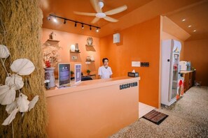 Un área de recepción con recepcionista, un mostrador, un ventilador de techo y un refrigerador.