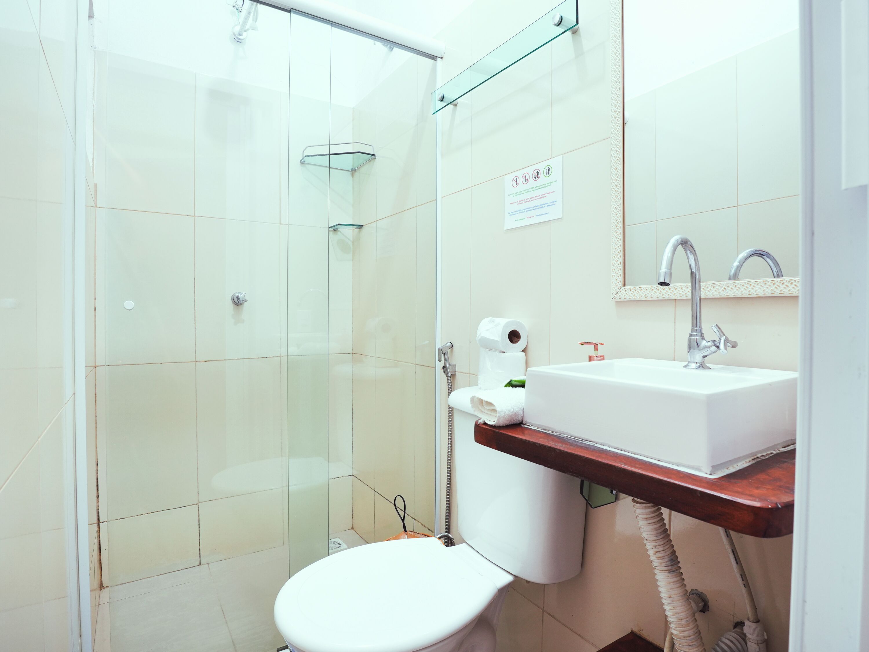 Un baño moderno con cabina de ducha de vidrio, inodoro blanco, lavamanos con espejo y toallero.