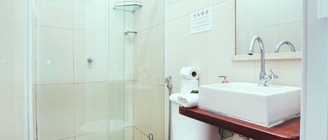 Un baño moderno con cabina de ducha de vidrio, inodoro blanco, lavamanos con espejo y toallero.